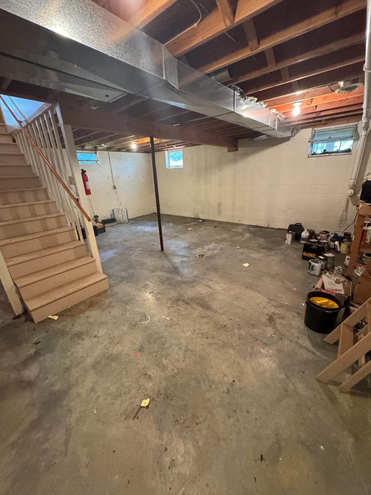 The same basement emptied to bare concrete after an estate cleanout, with only the homeowner's own paint cans left in the corner.