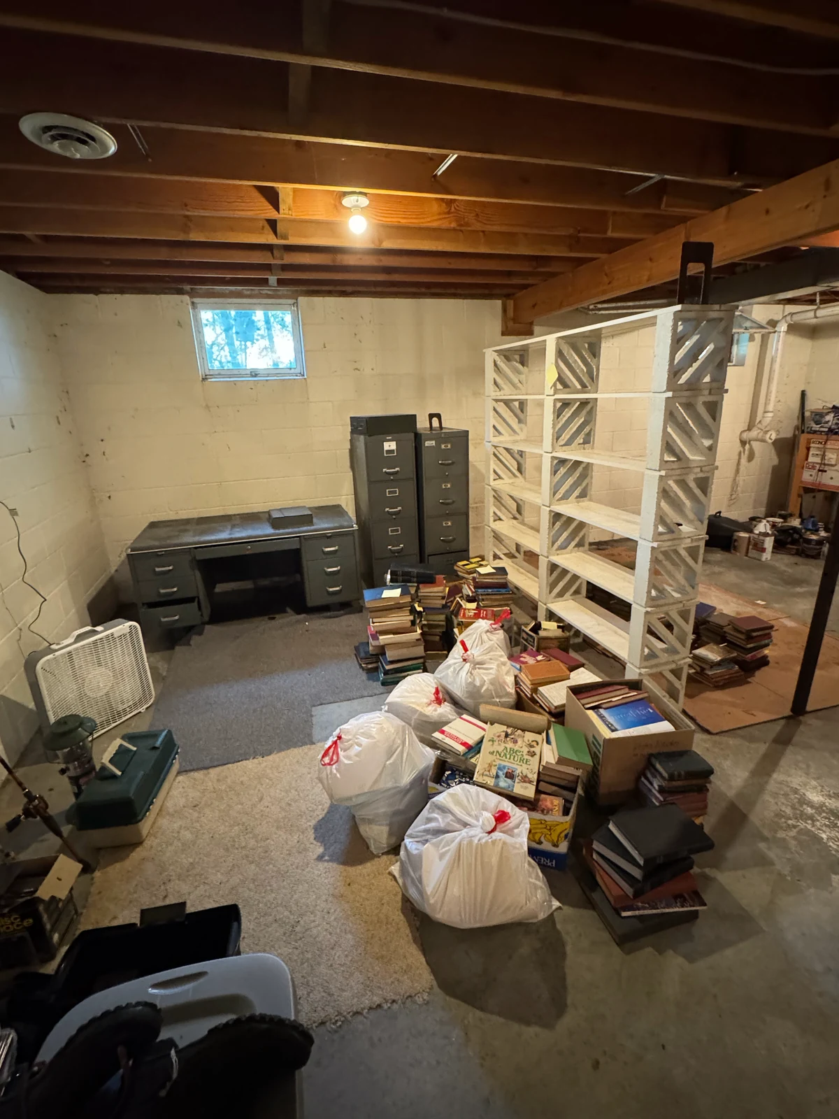 Basement room with a steel desk, filing cabinets and stacks of hardcover books bagged and boxed for removal during an estate cleanout in Grand Rapids, Minnesota.