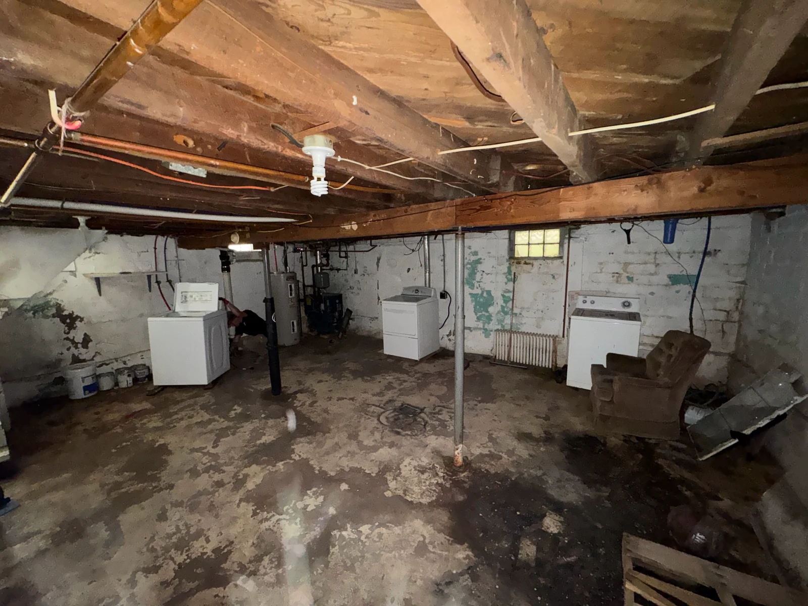 Older basement holding a washer, two dryers, a water heater and a cast iron radiator being disconnected for appliance removal in Grand Rapids, Minnesota.