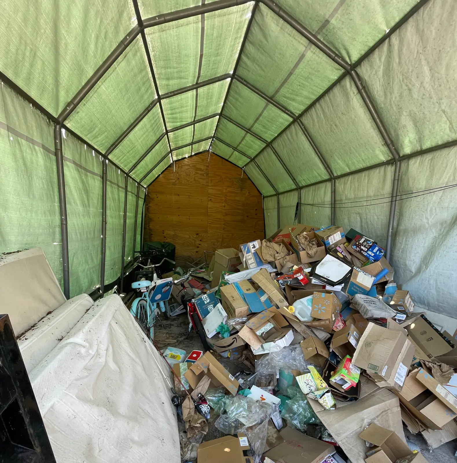 Portable fabric carport packed wall to wall with boxes, bags, a mattress and a bicycle before a full cleanout in Itasca County, Minnesota.