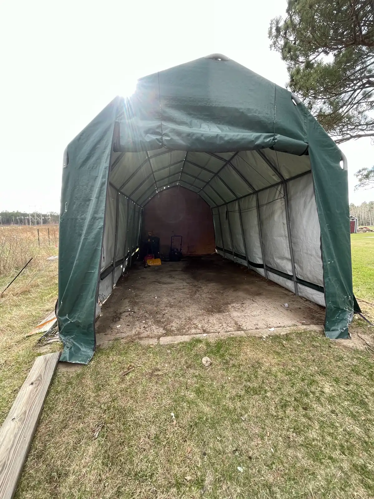 Empty portable fabric carport with a bare dirt and concrete floor after its contents were hauled away in Itasca County, Minnesota.